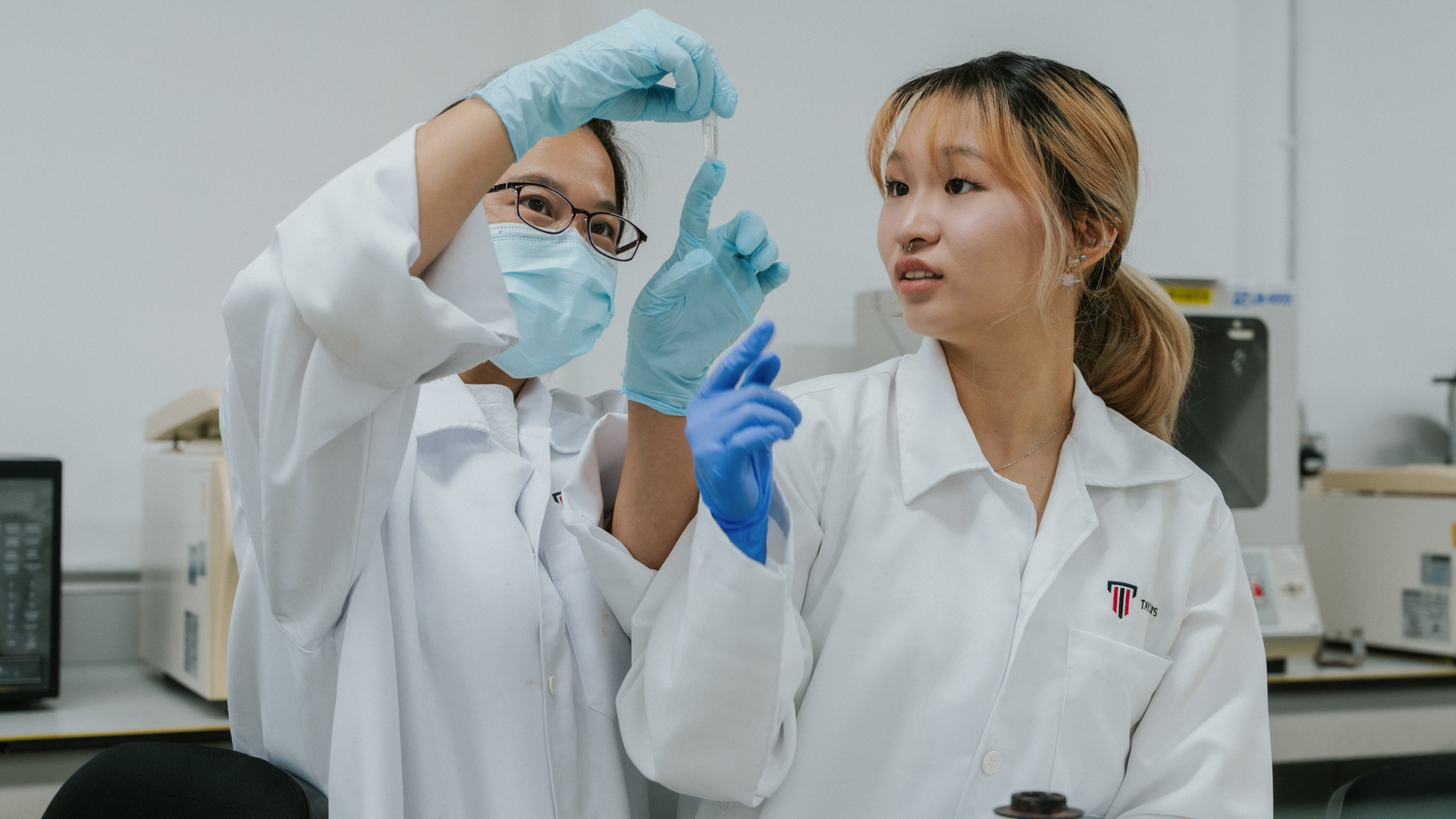 Two medical science students in collaborate in a laboratory, closely examining a small specimen vial.
