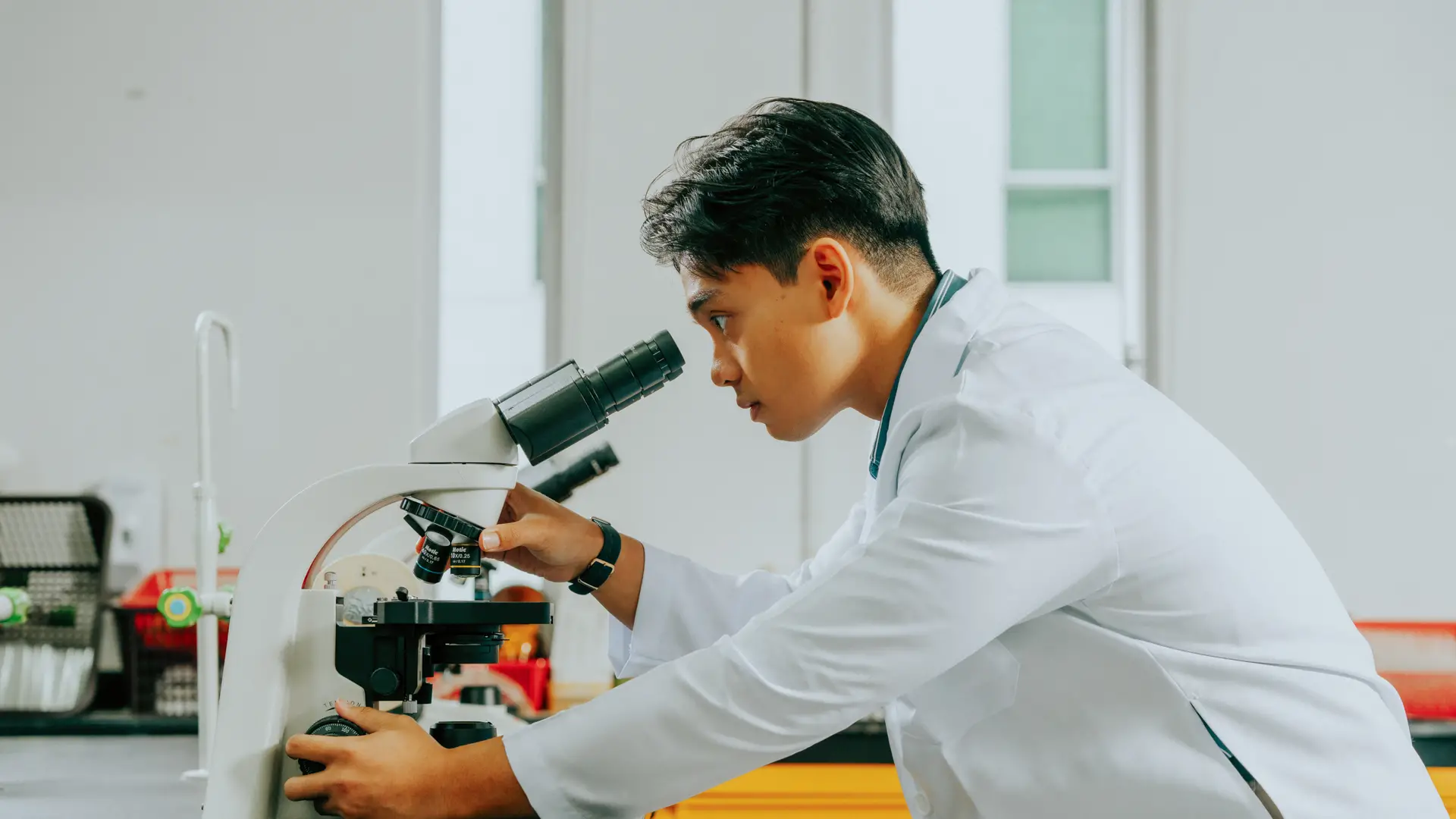  A medical student leans forward to focus and examine a specimen through a microscope in a laboratory.