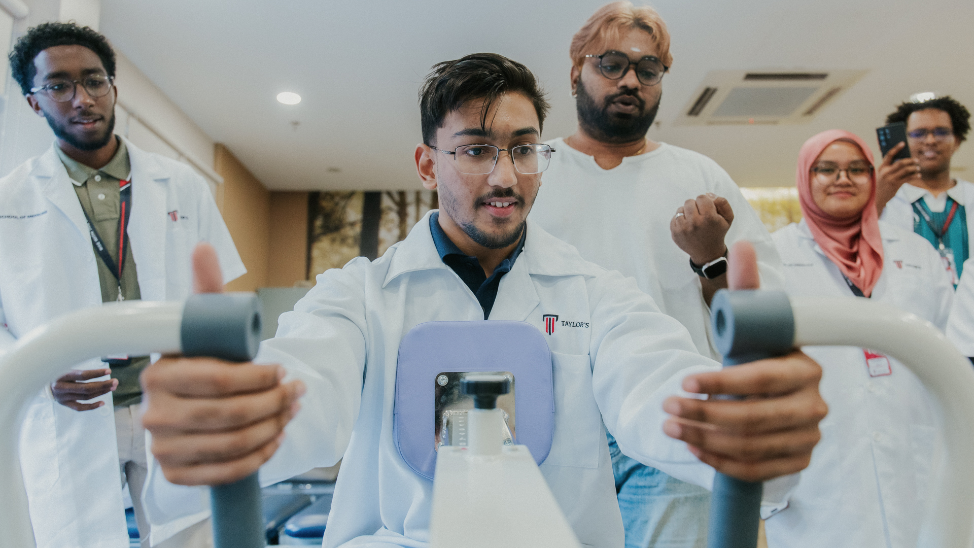  A group of Taylor's University medical students observe a peer demonstrating the use of a chest press rehabilitation machine.
