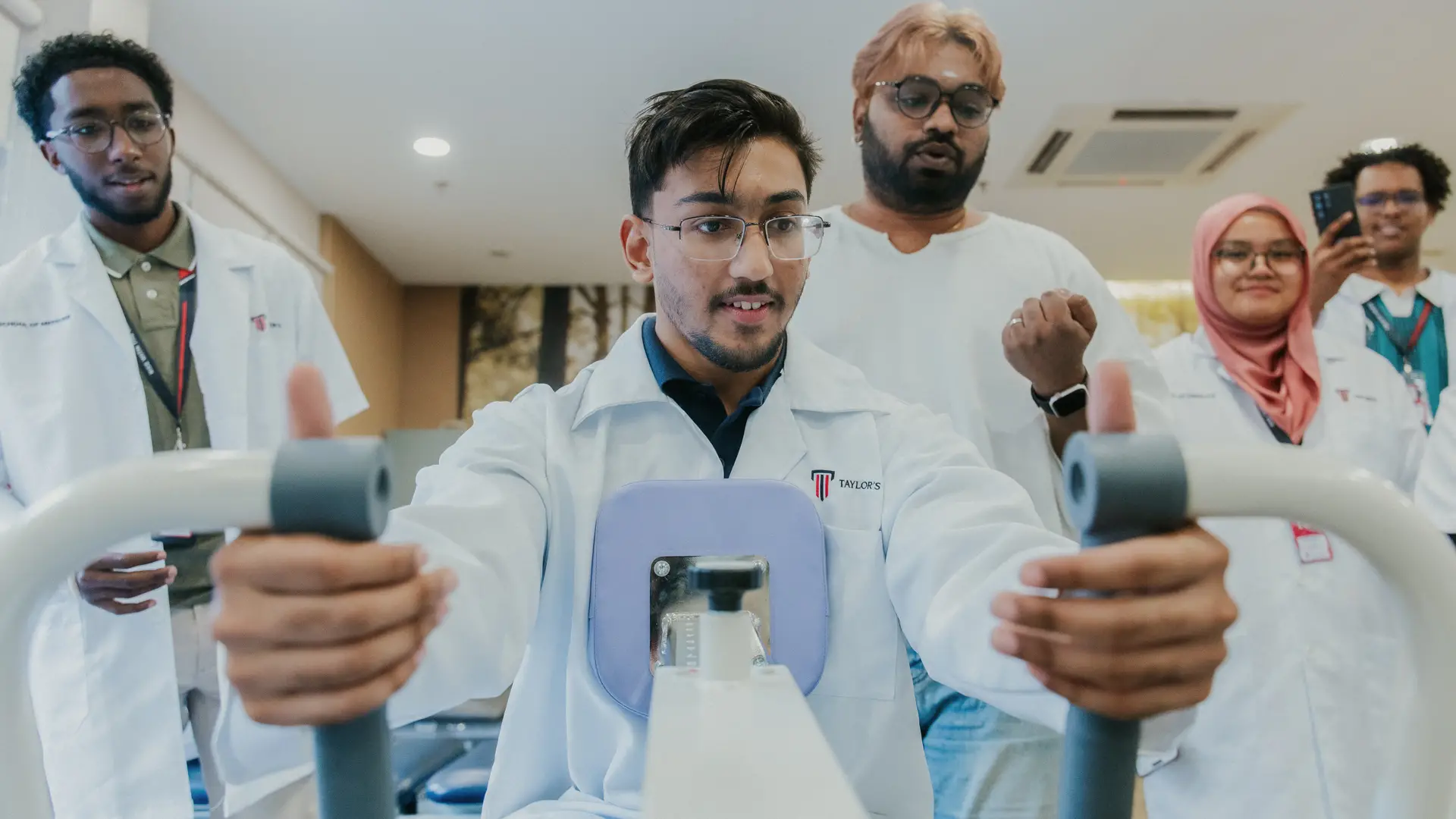  A group of Taylor's University medical students observe a peer demonstrating the use of a chest press rehabilitation machine.