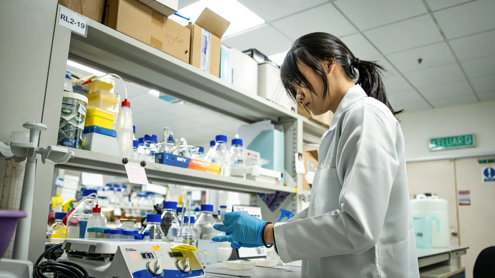  A pharmaceutical science student in a laboratory station filled with scientific equipment and glass bottles.