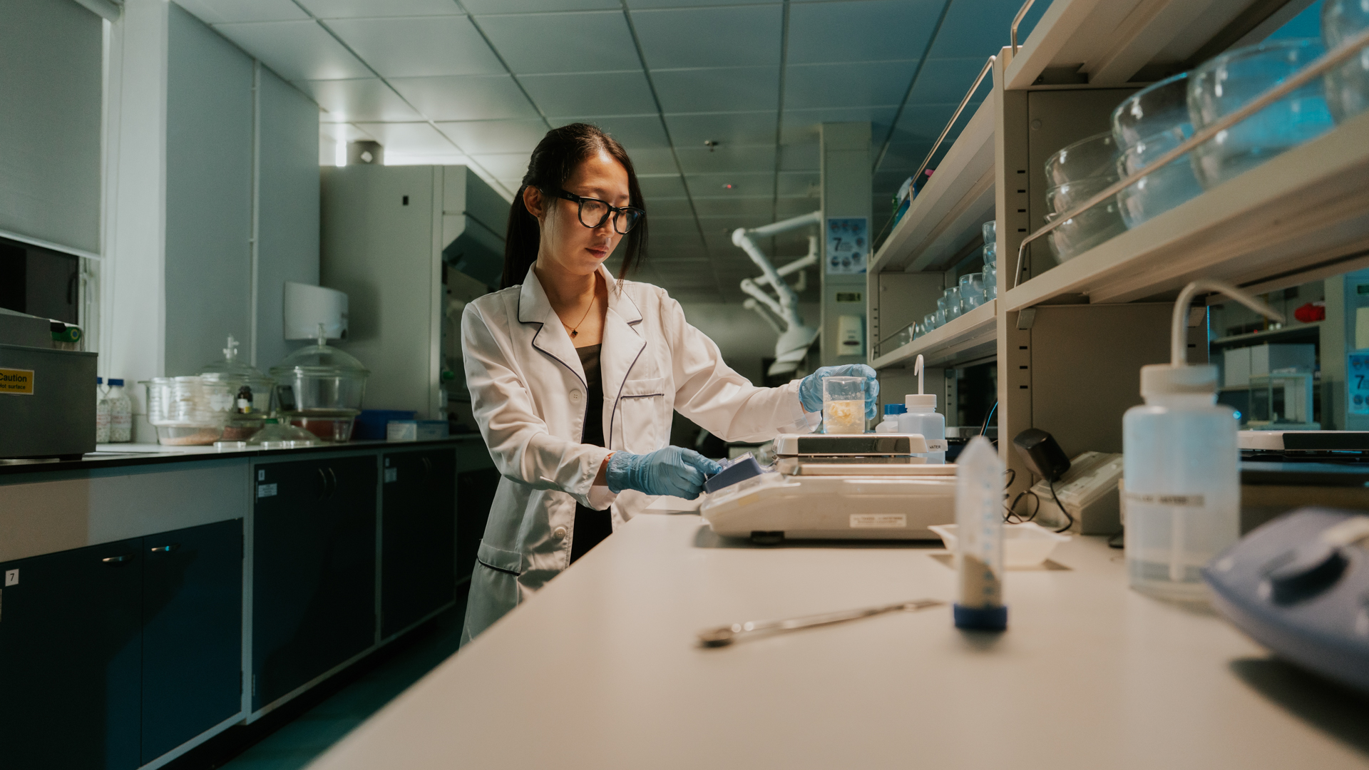 A pharmacy student next to a tablet compression machine in a laboratory setting.