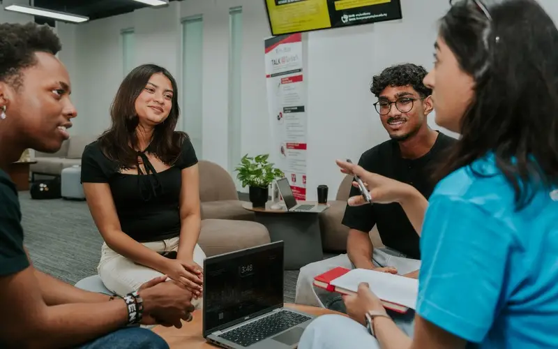Students chat in a relaxed small-group speaking session with a peer coach