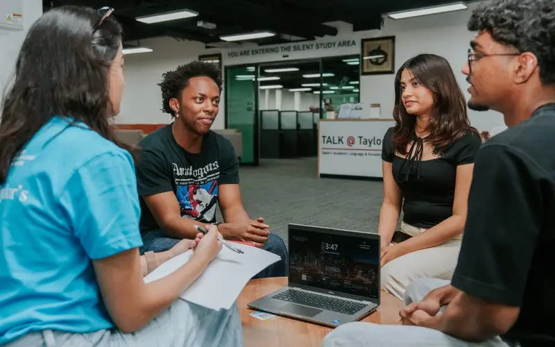 A small group of students works with a peer coach in the TALK@Taylor's Hub