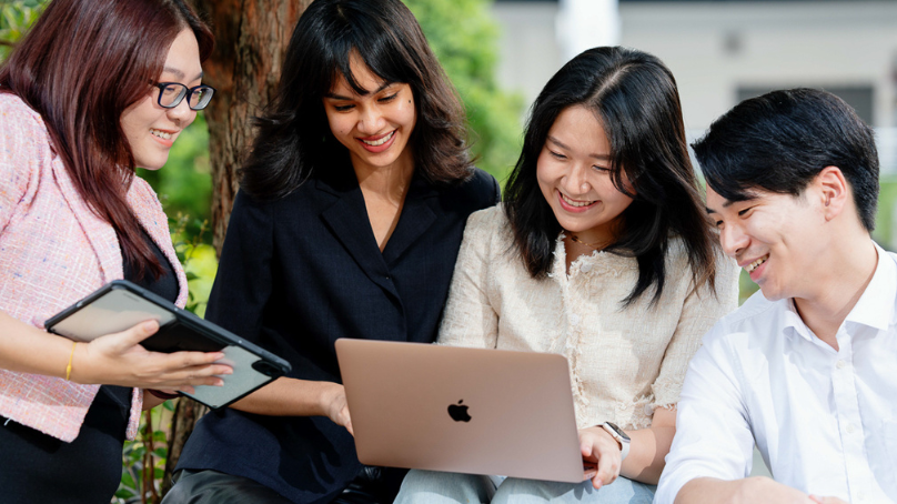 students gathered around a girl with a laptop on lap